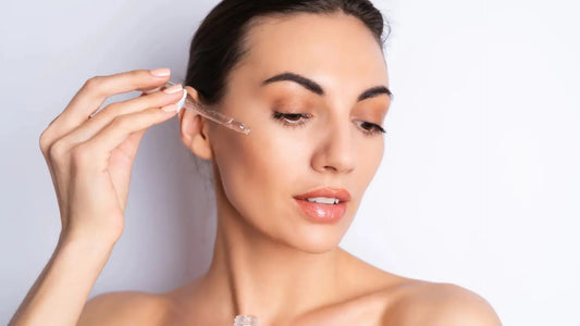 A woman applying a serum to her face with a glass dropper during a minimal skincare routine.