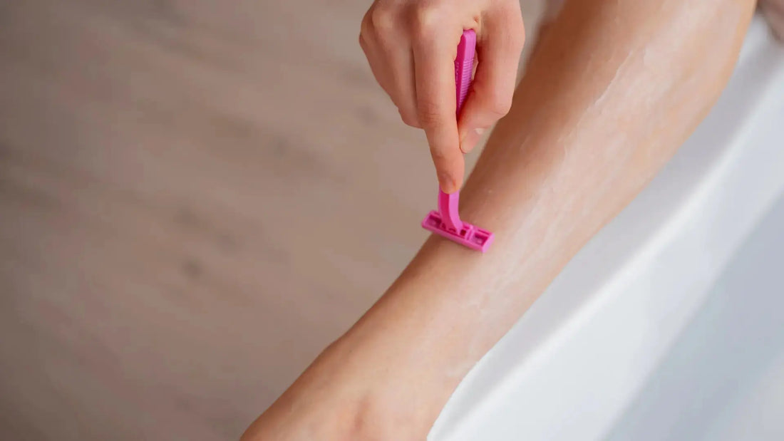 A hand holding a pink Razor while shaving smooth skin near the tub.