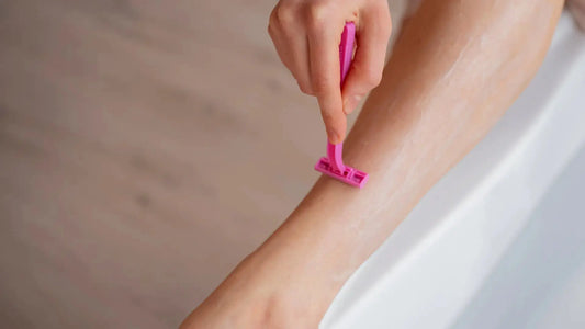 A hand holding a pink Razor while shaving smooth skin near the tub.