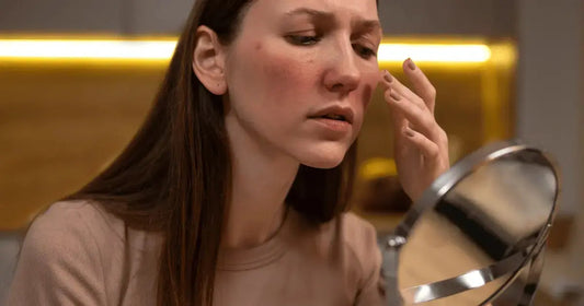 A concerned woman looking into a mirror, examining redness and skin irritation on her cheek from retinol burn.